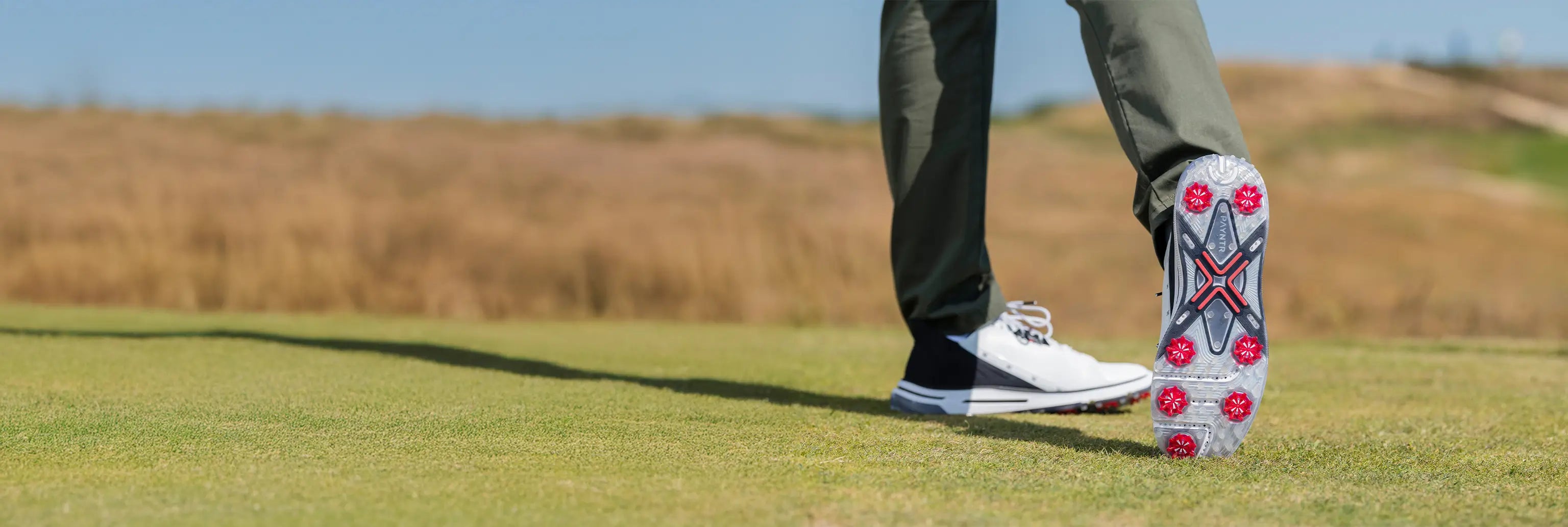 A person showing the underside of his golf shoe revealing the red pulsar golf spikes attached. 