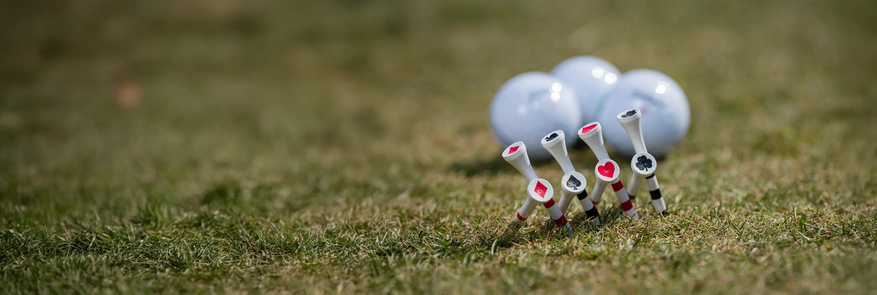 Eight specialized playing cards tees inserted into the ground with three golf balls positioned behind them. 