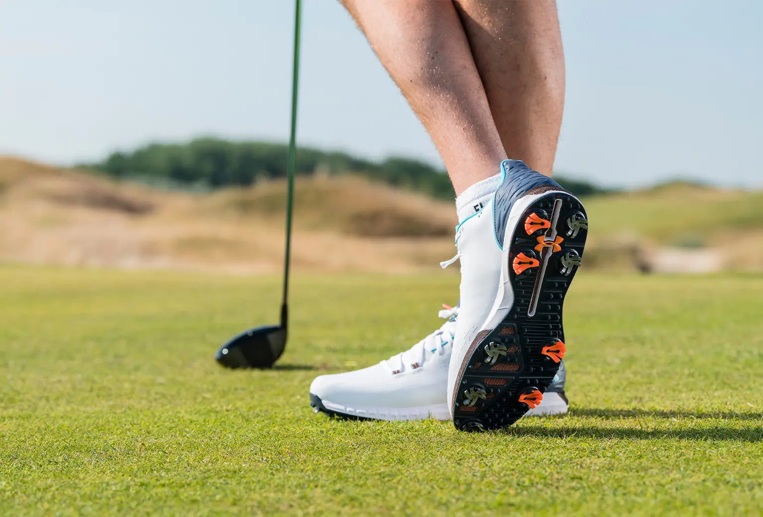A man showing his golf spikes underneath the bottom of his golf shoes. 