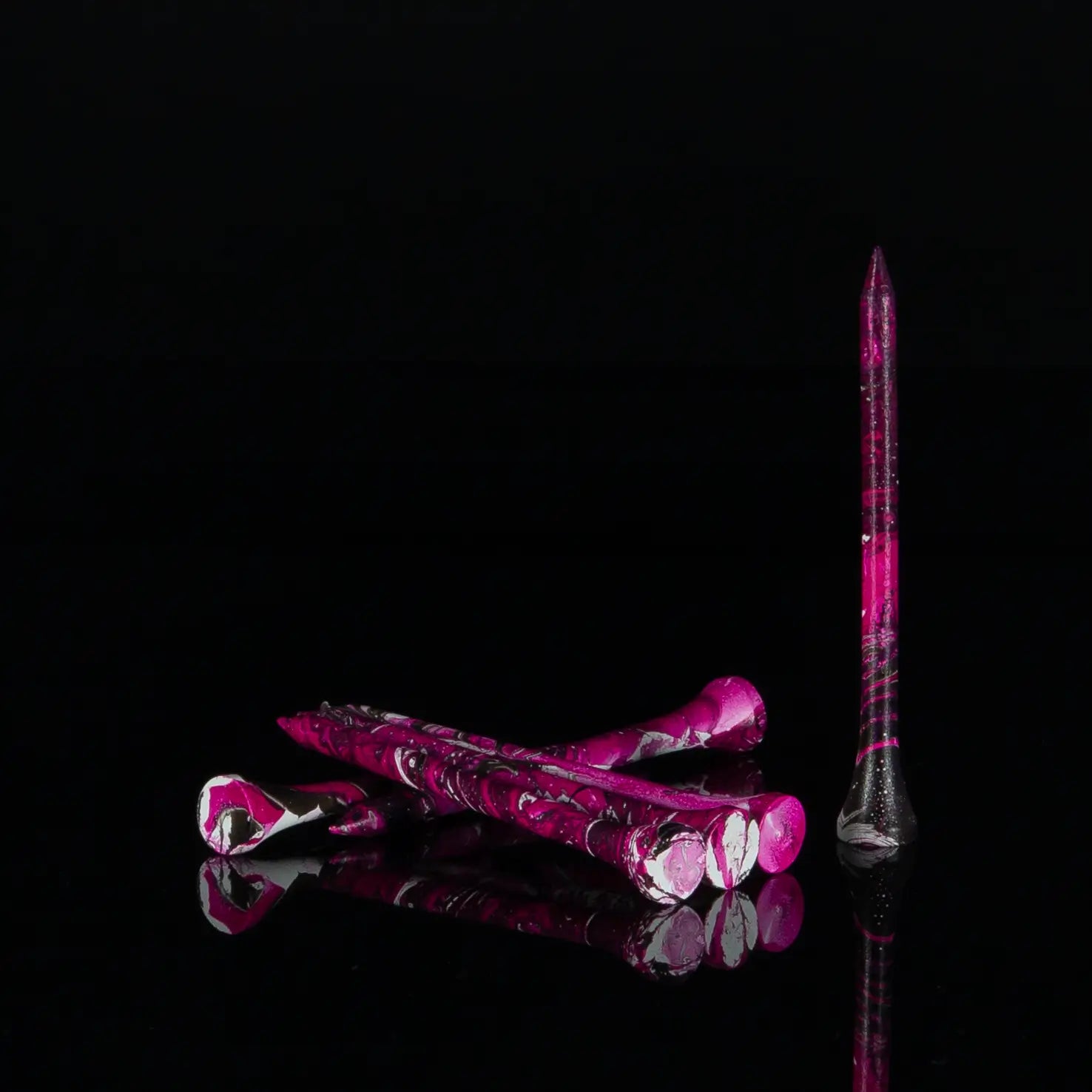 Five Neon Pink/Black paint splatter tees laying next to one another in a dark background. 