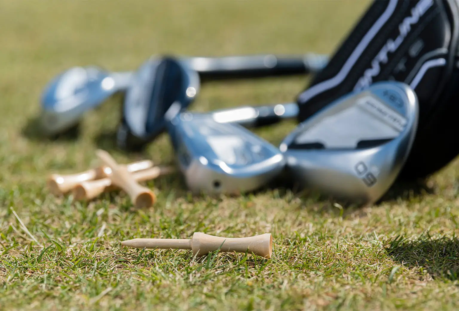Four wooden step tees laying on the ground next to a golf bag with different clubs. 