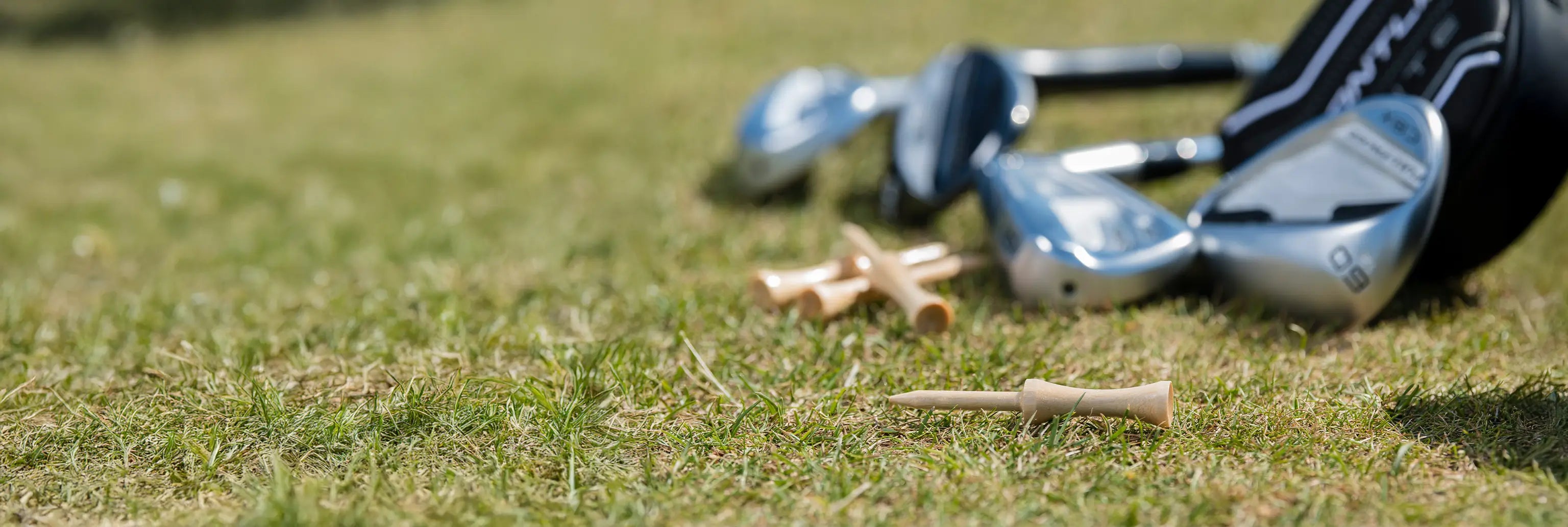 Four wooden step tees laying on the ground next to a golf bag with different clubs. 