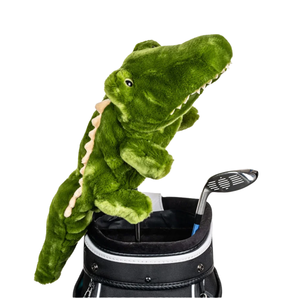 A green plush crocodile peeks from a golf bag, alongside a golf club.