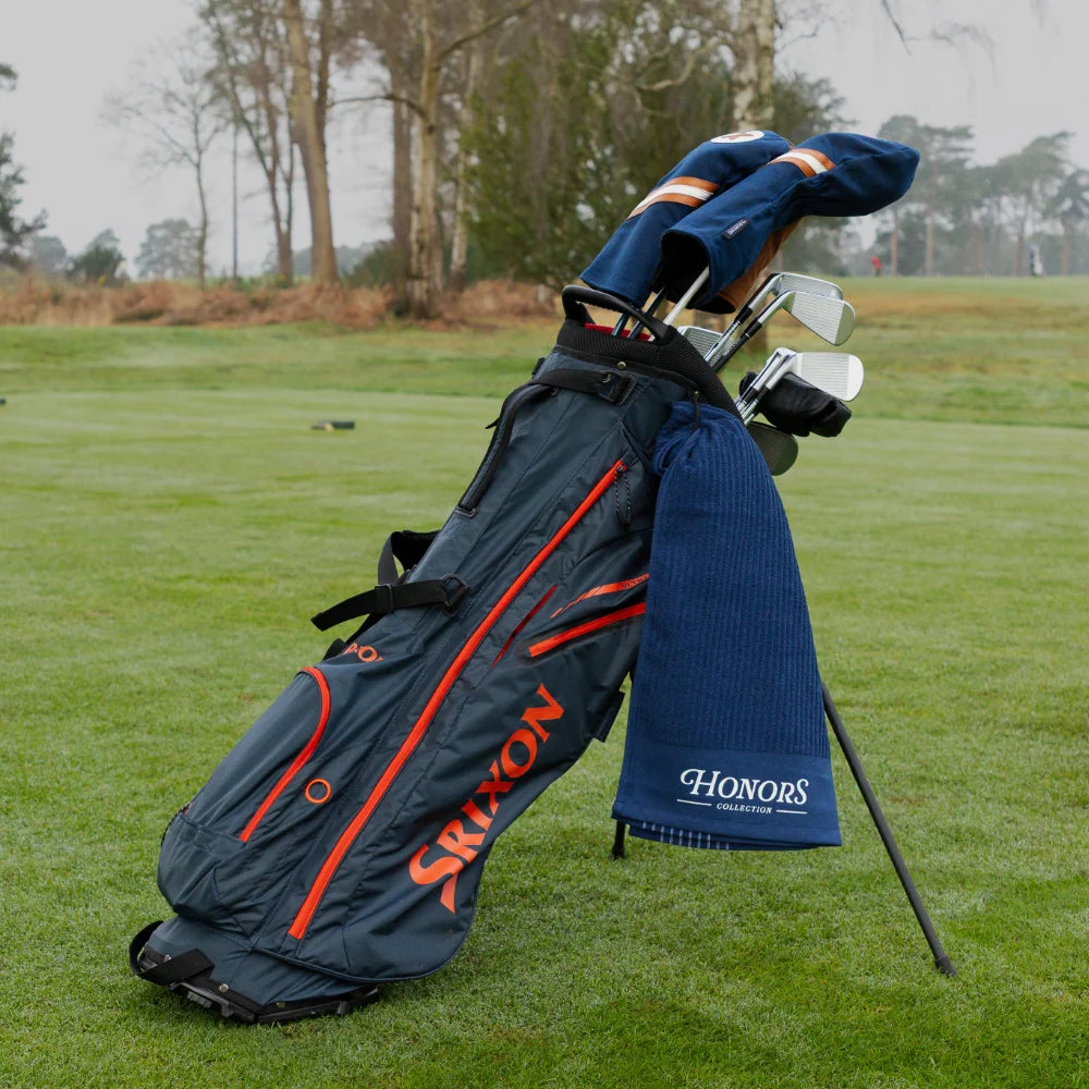 Honors Collection navy canvas driver and fairway headcovers resting in a golf bag with a matching towel on the course.