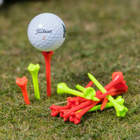 A titleist golf ball on an orange tee with colorful golf tees scattered around on grass.