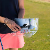 A person opens a packaging containing a Prosoft brush with white bristles, against a grassy background.