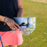 A person opens a packaging containing a Prosoft brush with white bristles, against a grassy background.