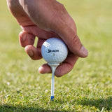Hand holding a Srixon golf ball on a tee against a grassy background