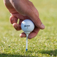 Hand holding a Srixon golf ball on a tee against a grassy background