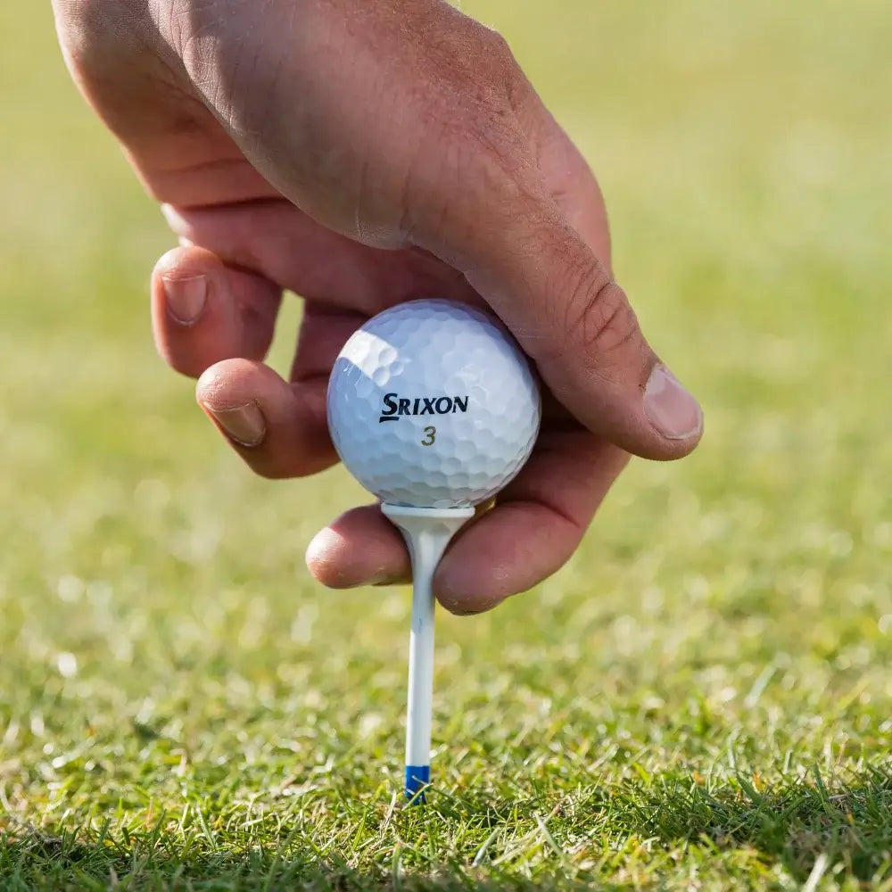Hand holding a Srixon golf ball on a tee against a grassy background