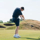 A man swinging a golf club on a golf course during a sunny day and wearing scorpion stinger golf spikes.