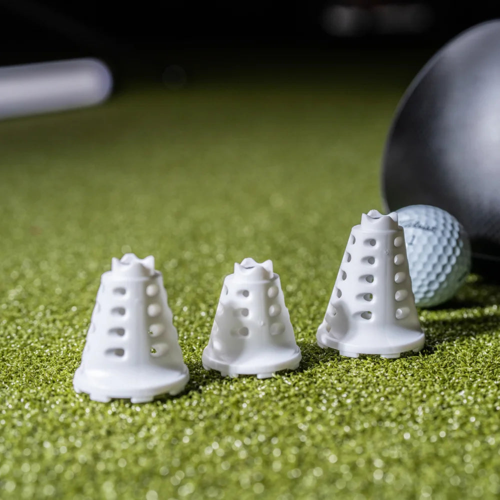 Pride Sports simulator golf tees in white on turf beside golf ball and driver head.