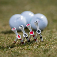 A close-up of golf tees with playing card symbols, and golf balls in the background on a grassy surface.