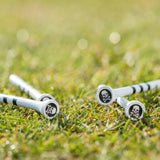 Four golf tees featuring skull and bones design on their tops, situated on green grass.