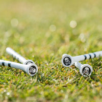 Four golf tees featuring skull and bones design on their tops, situated on green grass.