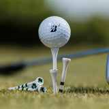 A bridgestone golf ball positioned on a tee, surrounded by additional golf tees, some with green stripes and clover designs, on grass.