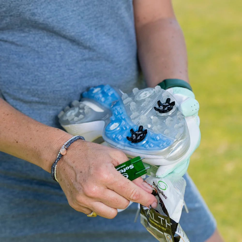 A person holding a golf shoe with a blue and white sole, adjusting stealth golf spikes, and holding a packet of golf spikes in their other hand.