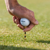 A hand placing a golf ball on a brown tee with black stripes on grass.