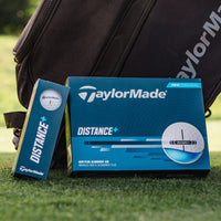 TaylorMade golf ball box and book on grass with a golf bag in the background