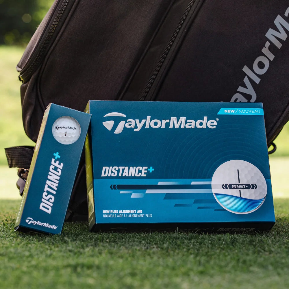 TaylorMade golf ball box and book on grass with a golf bag in the background