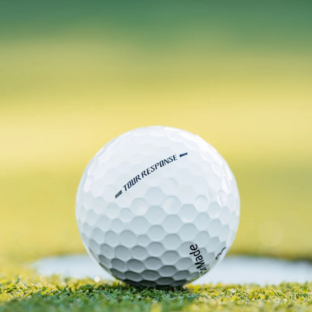 TaylorMade Tour Response golf ball resting on the green near the edge of the hole.