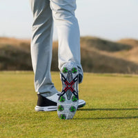 A close-up of a tour flex pro golf spikes on a shoe, with the foot in motion and wearing light-colored pants on a grass.
