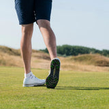 A close-up of a person's legs and golf shoes with green tour flex pro spikes walking on a grassy surface.