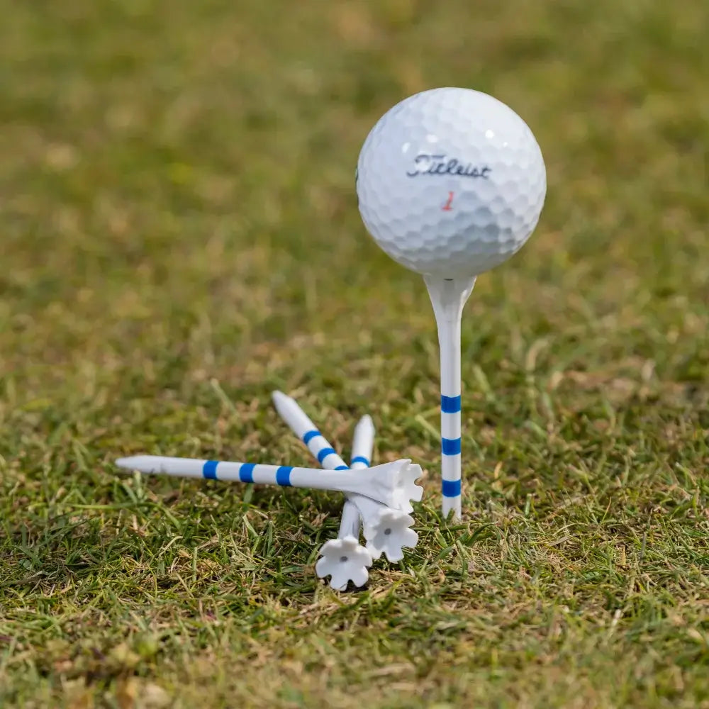 A white titleist golf ball on a tee with several blue-striped white golf tees on grass.
