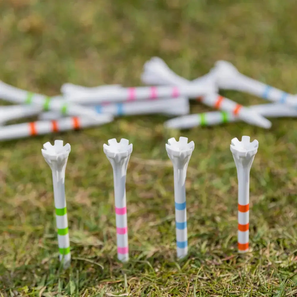 A collection of white golf tees in colorful stripes, some standing upright on grass with others scattered behind.