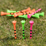 A collection of colorful golf tees in black stripes, some standing upright on grass with others scattered behind.