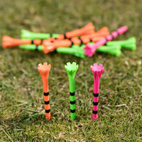 A collection of colorful golf tees in black stripes, some standing upright on grass with others scattered behind.
