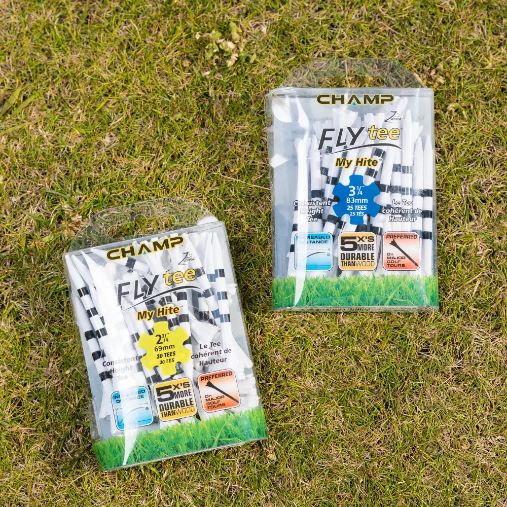 Two packages of golf tees on grass, labeled "champ fly tee," one containing 30 white tees with black stripes of 3¼ inches and the other 25 white tees with black stripes of 2½ inches, highlighting durability and preferred usage.