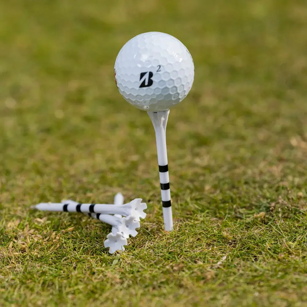 A white bridgestone golf ball on a tee with several white and black striped golf tees on grass.