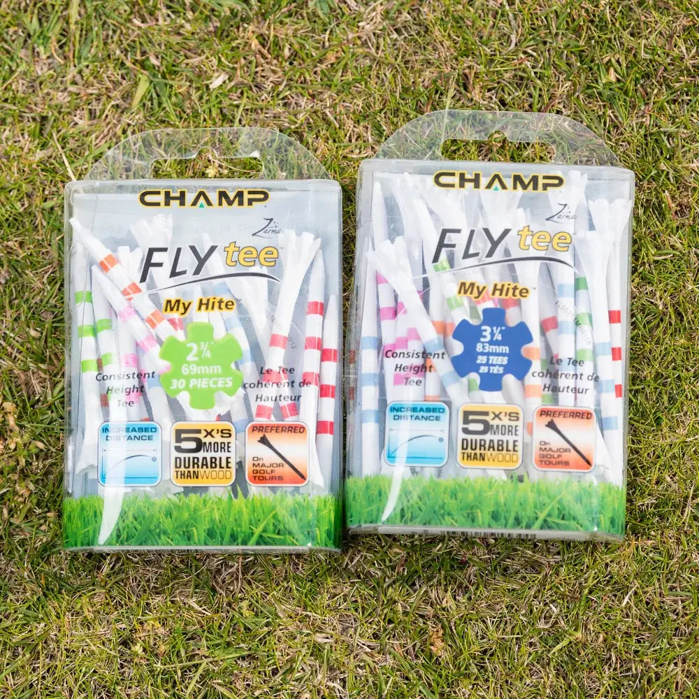 Two packages of golf tees on grass, labeled "champ fly tee," one containing 30 white tees with colorful stripes of 3¼ inches and the other 25 white tees with colorful stripes of 2½ inches, highlighting durability and preferred usage.