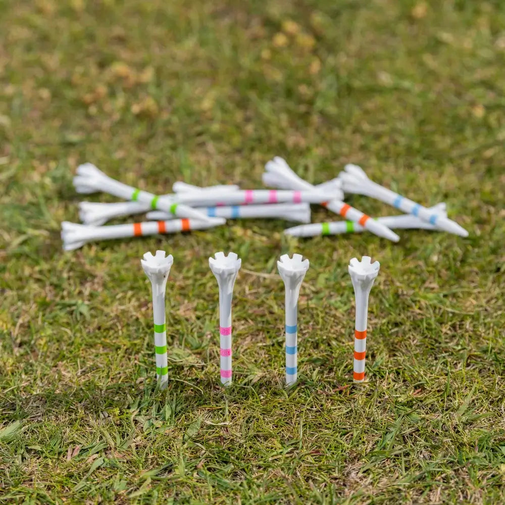 A collection of white golf tees in colorful stripes, some standing upright on grass with others scattered behind.